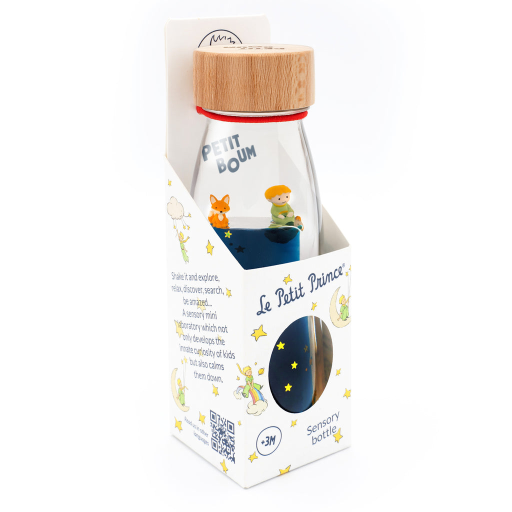 Packaging for a sensory bottle themed "Le Petit Prince." It features colorful illustrations of stars and characters, with a wooden cap and vibrant blue liquid inside. The mood is whimsical and playful.