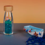 Sensory bottle with a whale and lighthouse next to a toy boat.