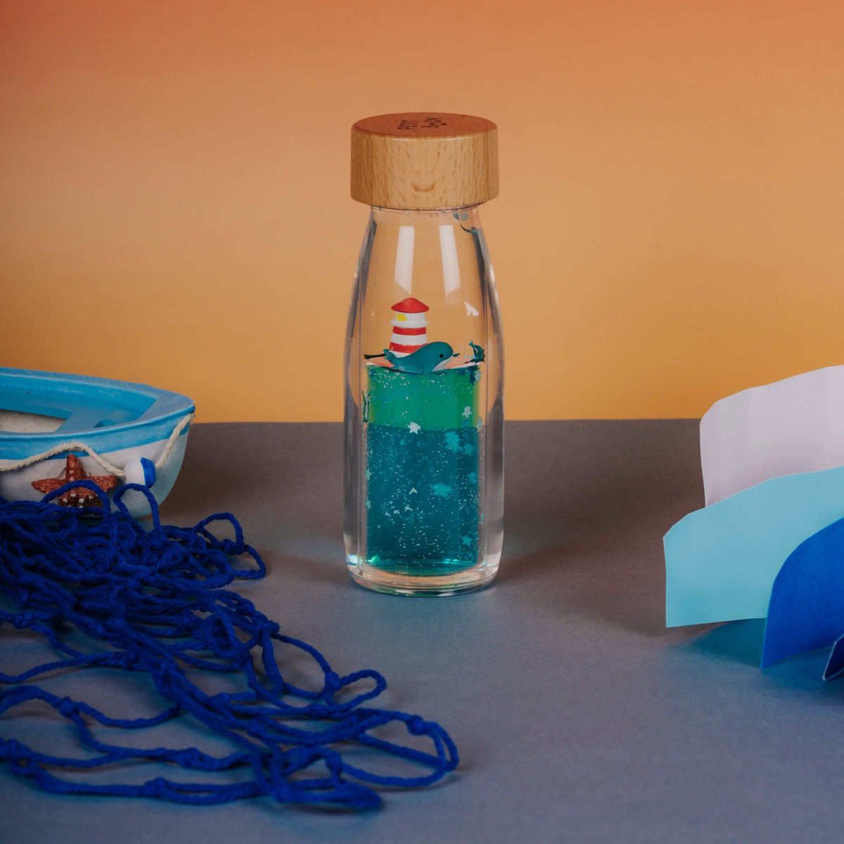 Sensory bottle featuring a whale and lighthouse, placed between a toy boat and paper waves.