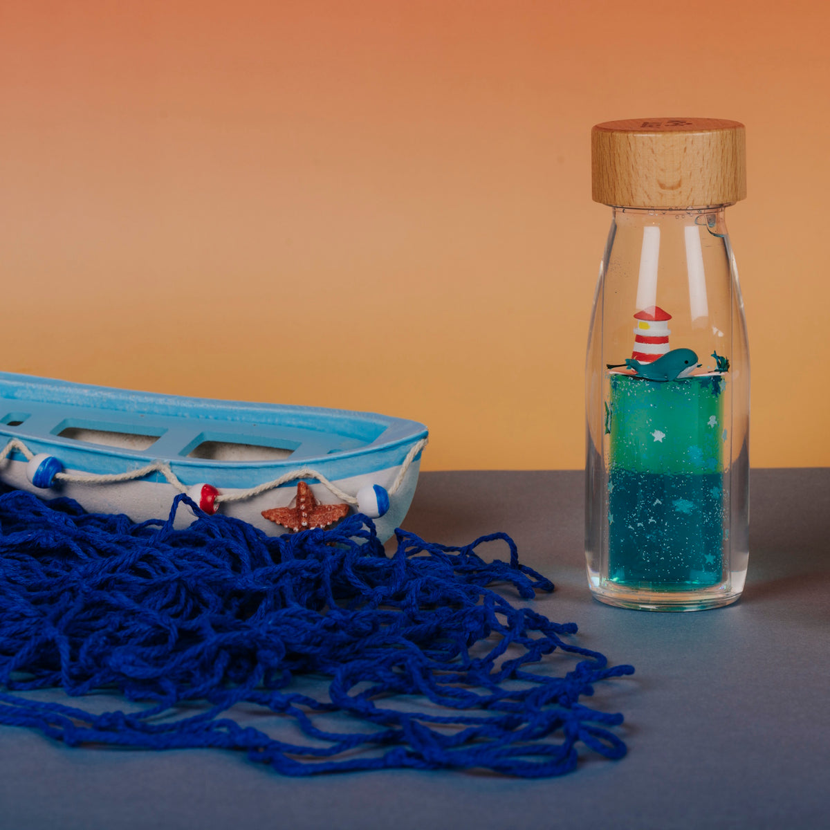Sensory bottle featuring a whale and lighthouse, placed beside a toy boat and blue fishing net.