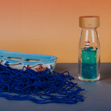 Sensory bottle featuring a whale and lighthouse, placed beside a toy boat and blue fishing net.