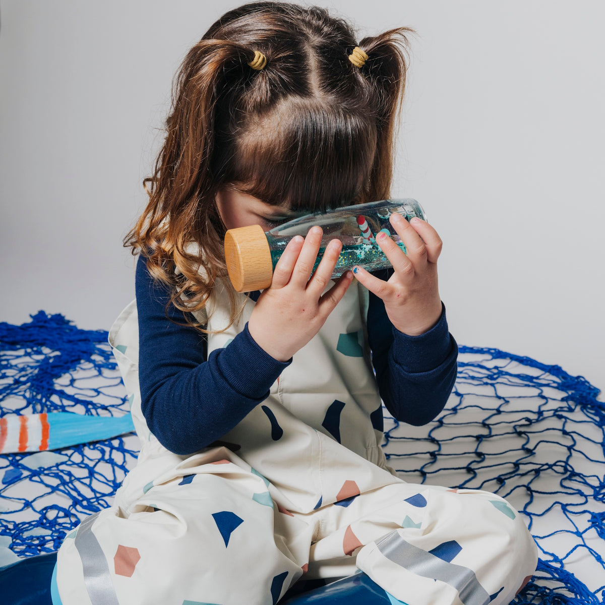 A young girl holding a sensory bottle up to her face to look through it.