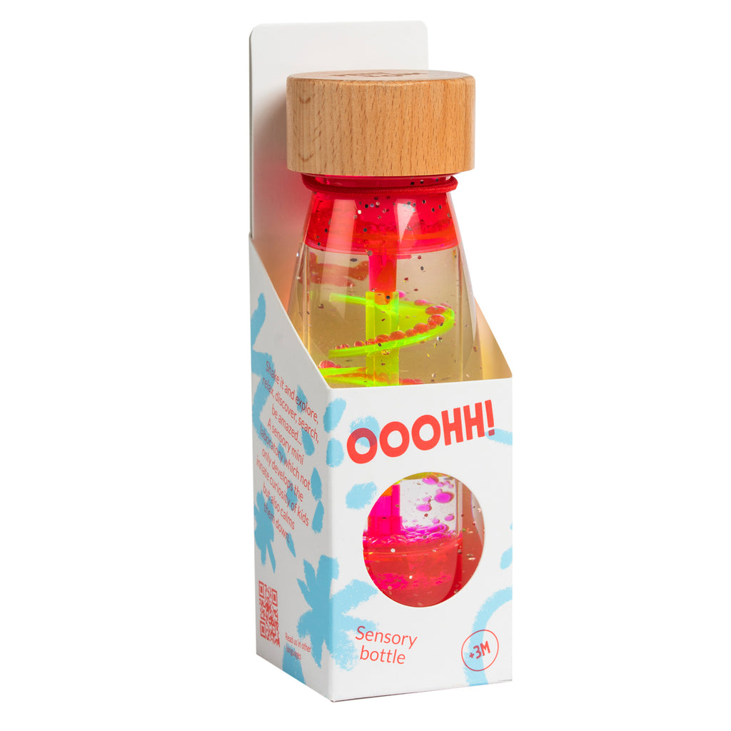 Wooden-capped sensory bottle in packaging. Clear with swirling neon liquid and small floating objects, labeled "OOOHH! Sensory bottle" for ages 3+.