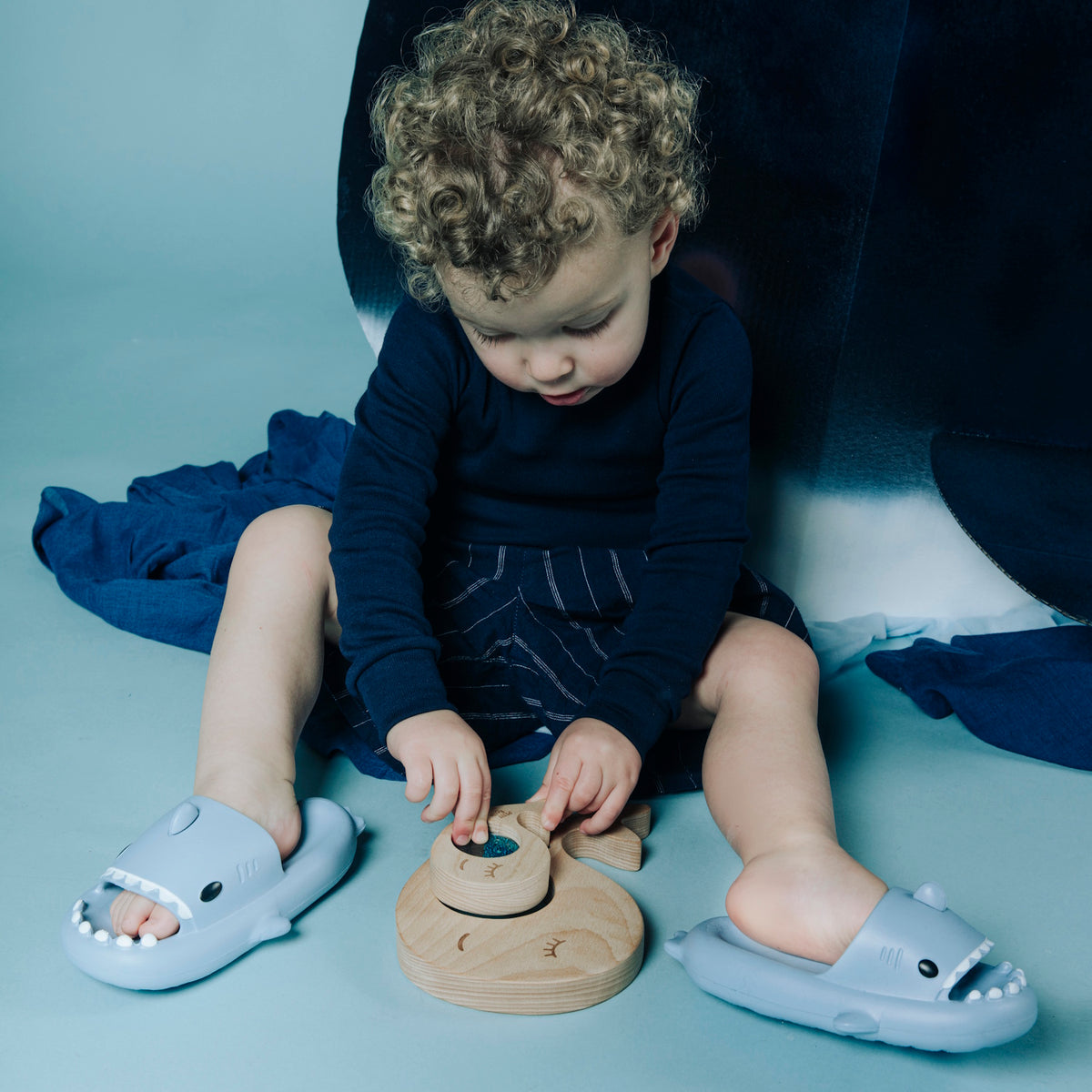 Toddler sitting on the floor and playing with the whale sensory puzzle while wearing shark slides.