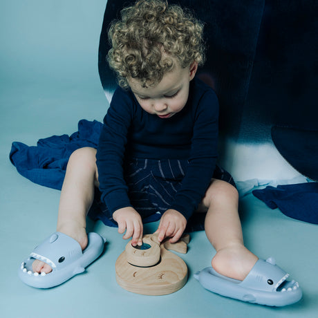 Toddler sitting on the floor and playing with the whale sensory puzzle while wearing shark slides.