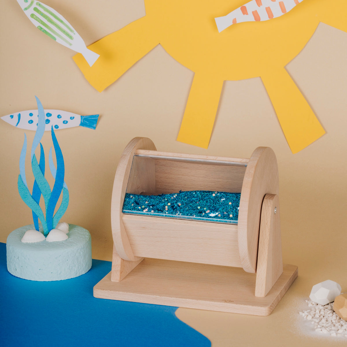 Wooden sensory roller toy filled with blue liquid, set against an ocean-themed backdrop.