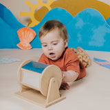 Baby lying on their tummy and playing with a wooden sensory roller.