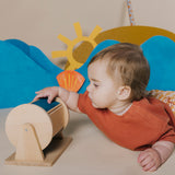 Baby lying on their tummy and touching a wooden sensory roller.
