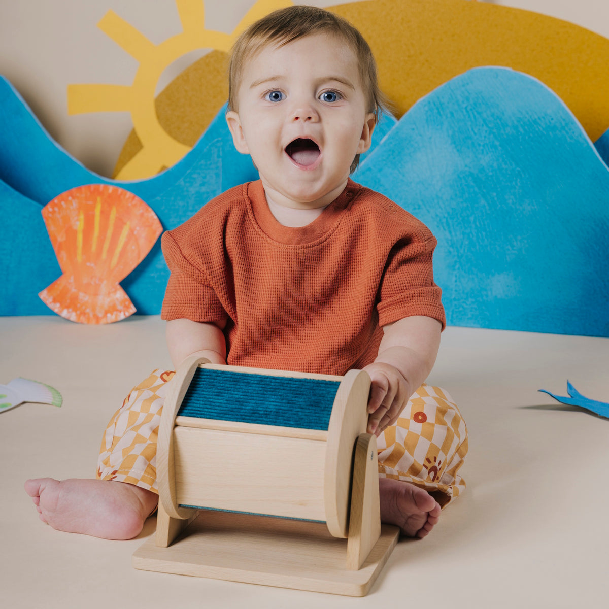 Baby sitting up and playing with a wooden sensory roller.