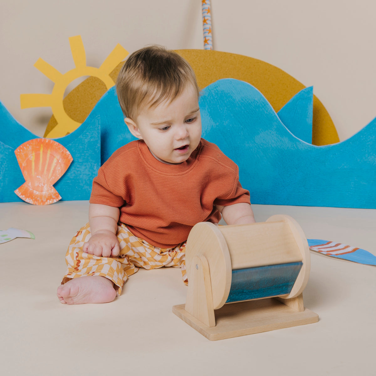 Baby sitting on the floor and looking down at a wooden sensory roller.