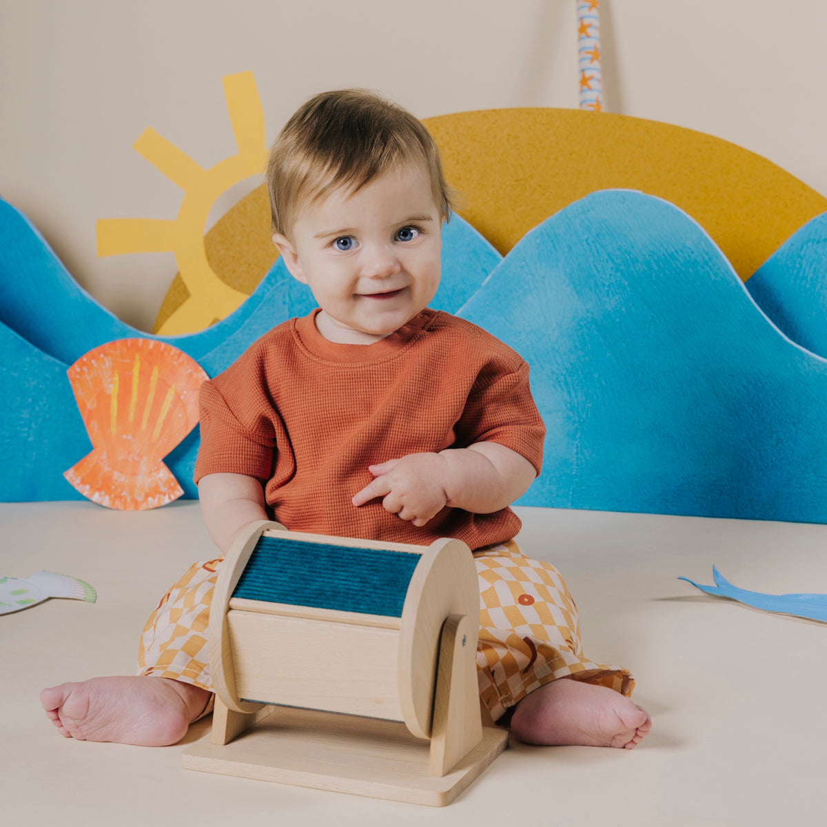 Baby sitting on the floor and pointing at a wooden sensory roller.