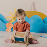 Baby sitting on the floor and looking down at a wooden sensory roller.