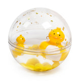 A clear acrylic sphere containing two floating yellow rubber ducks, with gold bubbles floating around them. The scene is playful and cheerful.