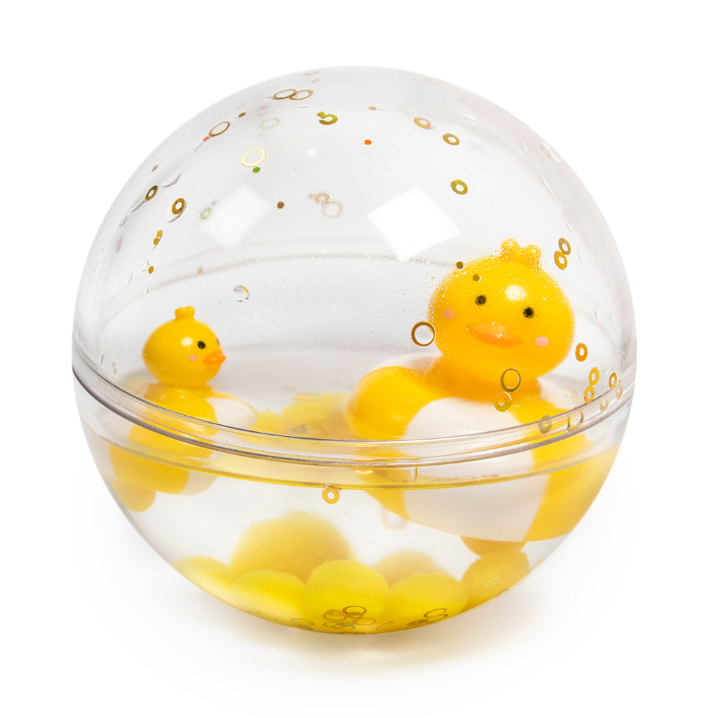 A clear acrylic sphere containing two floating yellow rubber ducks, with gold bubbles floating around them. The scene is playful and cheerful.