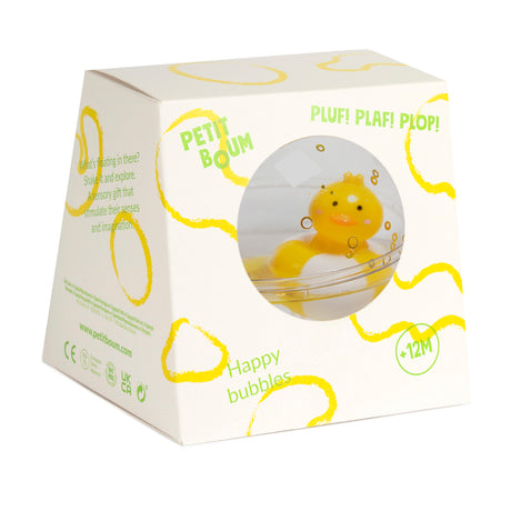 White box with a circular window revealing a floating yellow duck in clear liquid. Box features yellow wavy lines, text reads "Petit Boum," "Happy bubbles," and is for ages 12 months and up.