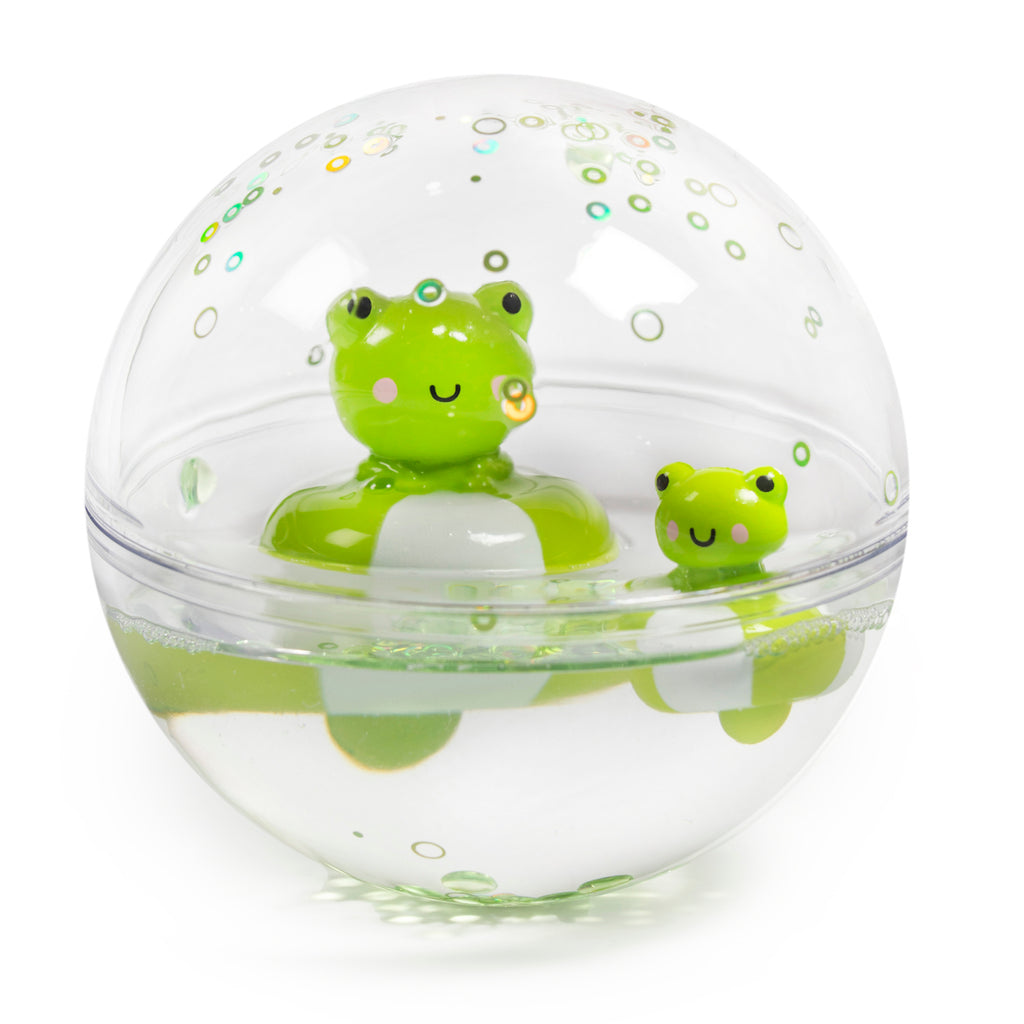 A clear sphere containing two smiling green frog toys floats in water, surrounded by air bubbles. The scene is playful and whimsical.