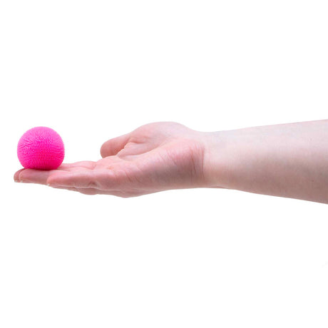 A small, fuzzy pink sensory ball resting on the fingertips of an open hand against a white background.