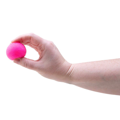 A hand holding a small, textured bright pink stress ball between the fingers against a white background.
