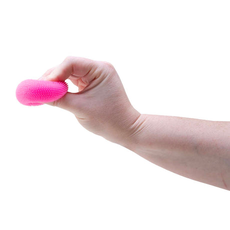 A hand squeezing a small, textured pink rubber stress ball against a plain white background.