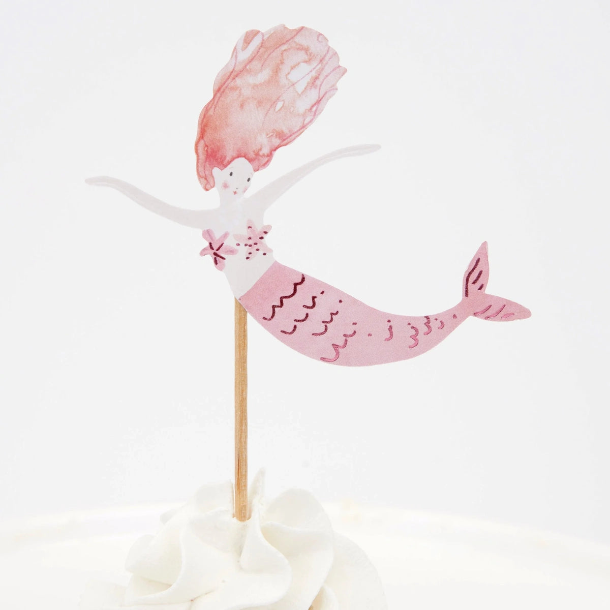 Watercolor pink mermaid cupcake topper with orange-pink hair, placed in white frosting against a plain background.