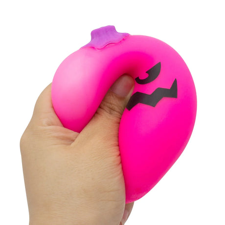 Hand squeezing a pink NeeDoh Jack-Glow Lantern stress toy, showing its squishy texture and jack-o-lantern face.