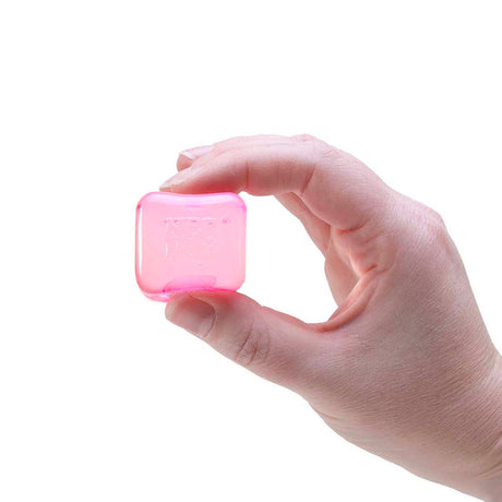 A hand pinching a small, translucent pink ice cube fidget toy against a white background.
