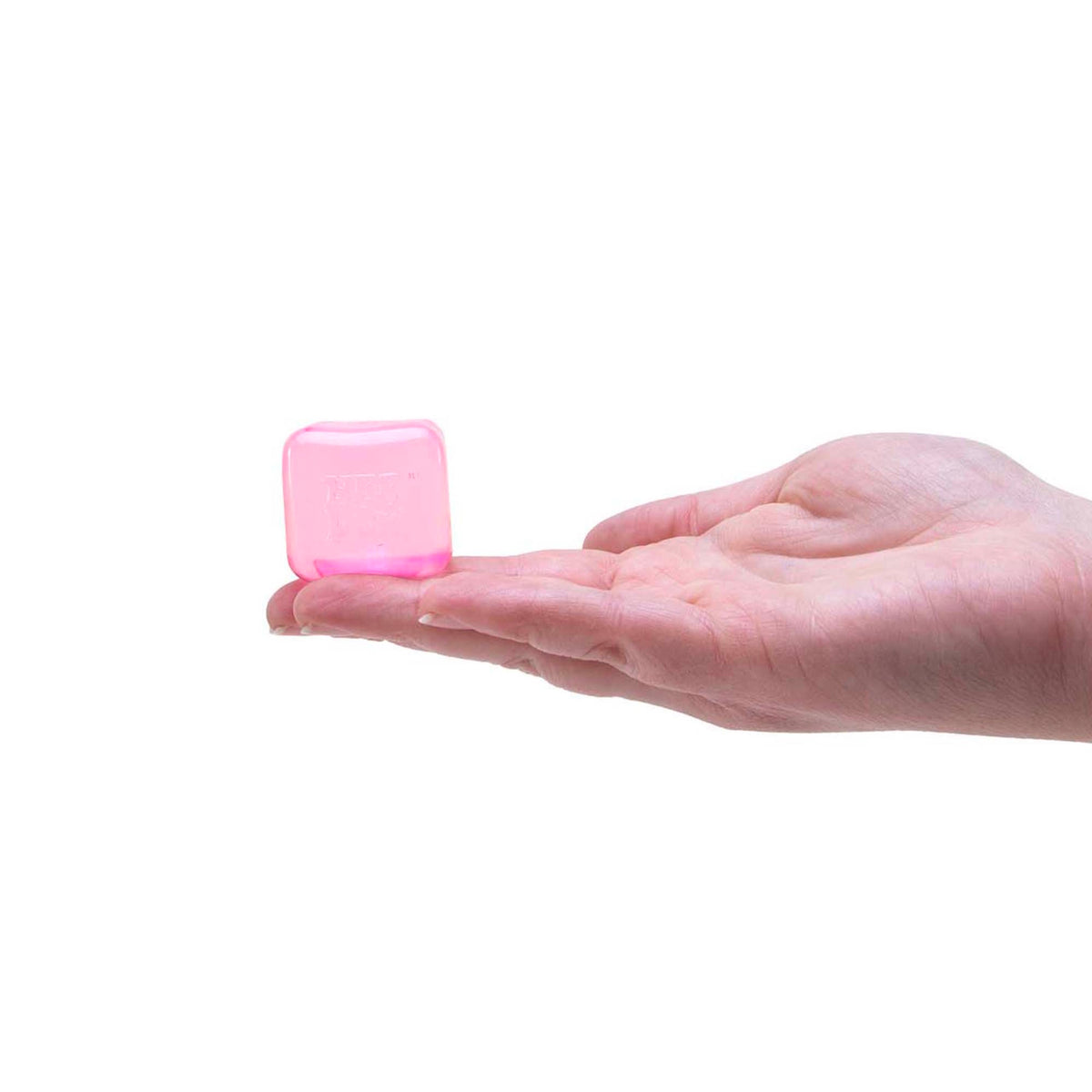 A person's open hand holding a small, translucent pink ice cube-shaped Teenie NeeDoh squishy toy.