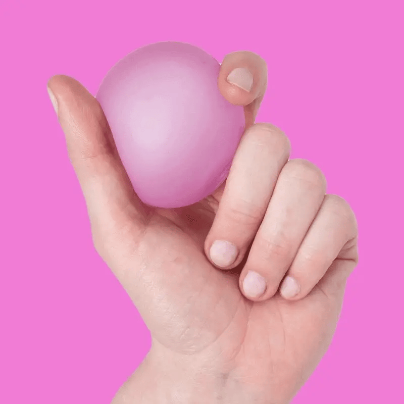 A hand holding and squeezing a squishy pink stress ball against a bright pink background.