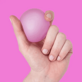 A hand holding and squeezing a squishy pink stress ball against a bright pink background.