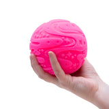 A hand holding a textured, bright pink sensory ball with fuzzy patterns against a white background.