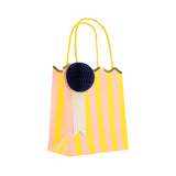Pink and yellow striped party bag with a scalloped gold edge, yellow handles, and a navy blue honeycomb paper pom-pom.