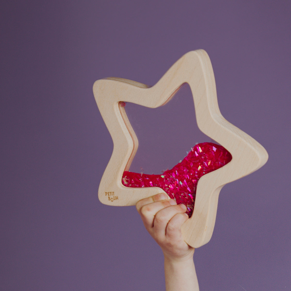 A child holding up the wooden star-shaped sensory toy filled with pink glitter.