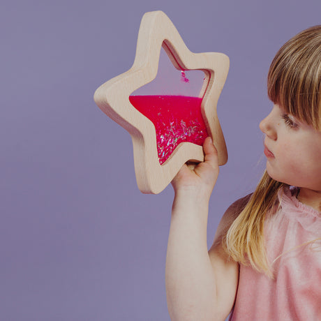 A young girl curiously looking through the pink glitter-filled star-shaped sensory toy.
