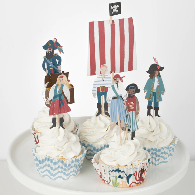 Cupcakes with white frosting and pirate themed toppers and liners on a white plate.