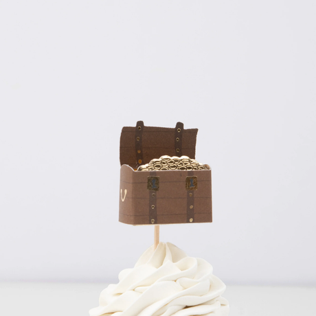 Open treasure chest filled with gold coins cupcake topper on a wooden pick in swirled white frosting.