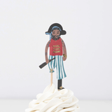 Pirate crew member topper in a red shirt and striped pants on a wooden pick in swirled white frosting.