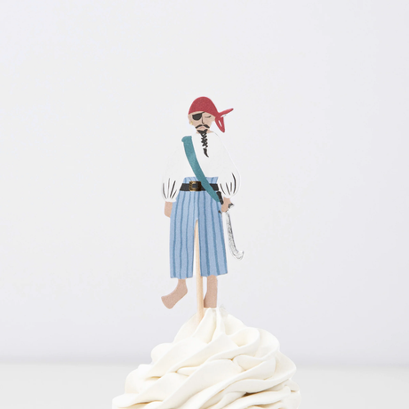 Pirate crew member topper in a red headscarf and striped pants on a wooden pick in swirled white frosting.