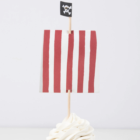 Red and white striped sail and skull flag cupcake topper on a wooden pick in swirled white frosting.