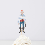 Pirate crew member topper in a striped shirt and red belt on a wooden pick in swirled white frosting.