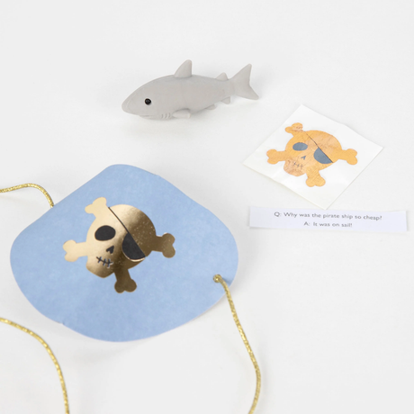 Light blue pirate eye patch, toy shark, sticker, and joke slip unwrapped from a surprise ball.