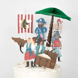 A cake decorated with pirate-themed toppers, a ship's sail, a palm tree, and a treasure chest.