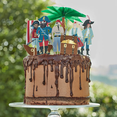Chocolate drip cake topped with pirate figures, a treasure chest, and a paper palm tree.