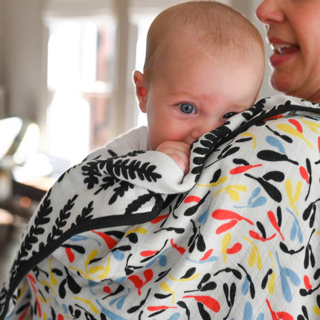 Baby looking over an adult's shoulder while wrapped in a patterned muslin blanket.