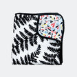 Folded muslin blanket with a black fern pattern and a colorful botanical underside.