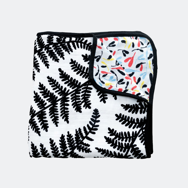 Folded muslin blanket with a black fern pattern and a colorful botanical underside.