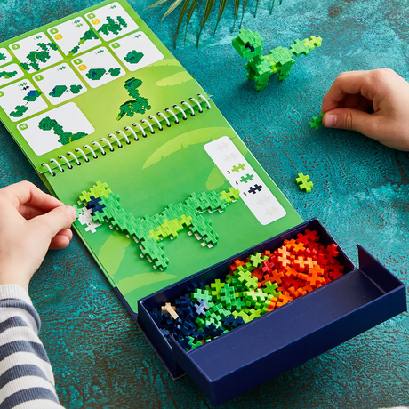 Child building a green dinosaur with Plus-Plus pieces on a dinosaur-themed activity pad.
