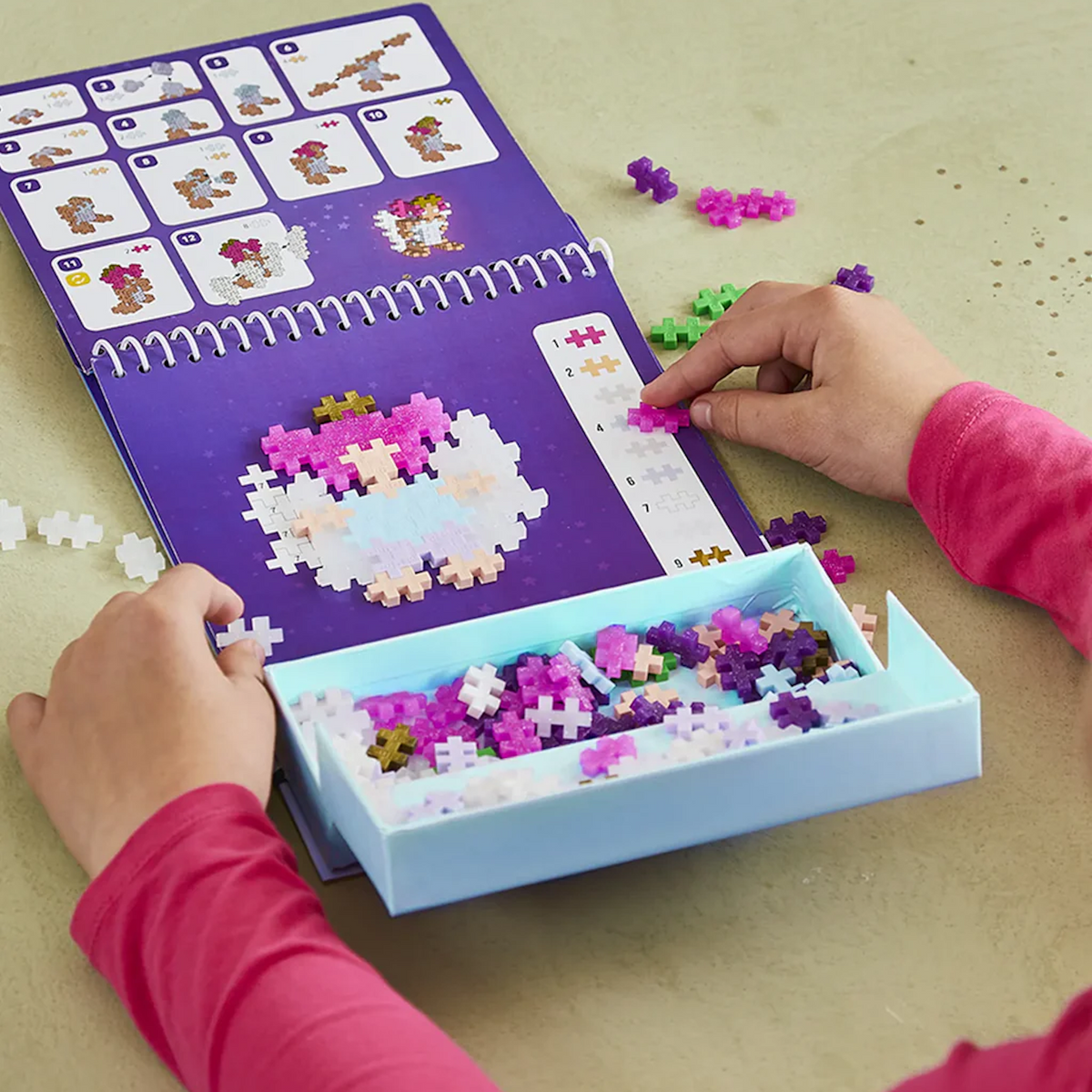 Child using a Plus-Plus Enchanted Forest activity pad to build a 2D fairy figure with colorful interlocking blocks.