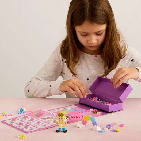 A young girl building fairytale figures with a Plus-Plus activity pad and colorful building blocks.