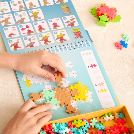 Child playing with a Plus-Plus activity pad to build a colorful puzzle turtle and figures on a light surface.