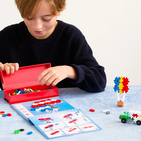 Child using a Plus-Plus activity pad to build a colorful hot air balloon and truck with interlocking puzzle blocks.